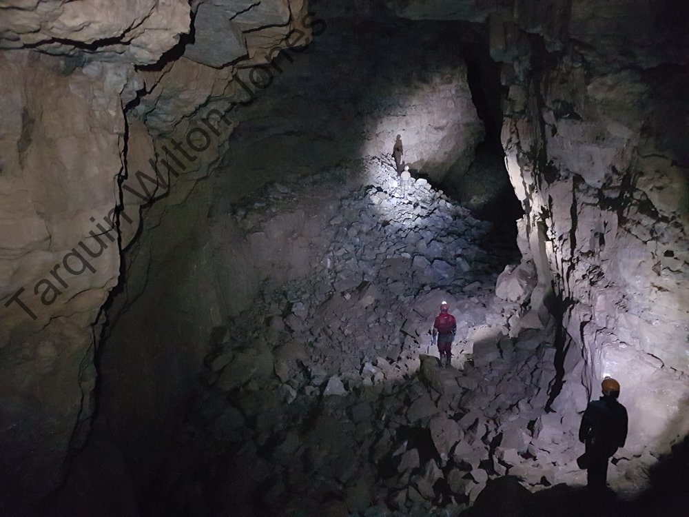 In the depression in the floor to the left of the caver in red.